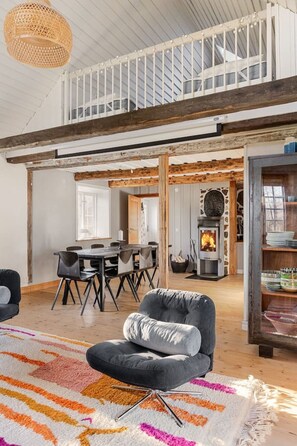 Un loft espacioso con techo alto, vigas de madera a la vista, comedor, chimenea y zona de estar acogedora.