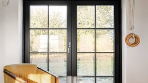 Een kamer met een grote schuifdeur van glas, een houten stoel, een bank en een hanglamp.