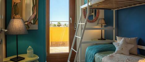 Un dormitorio con literas, un escritorio con lámpara, un cuadro y vistas al exterior.