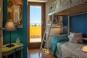 A bedroom with bunk beds, a desk with a lamp, a painting, and a view of the outside. - Panoramic penthouse on the Gulf of Alghero 2 (Alghero)
