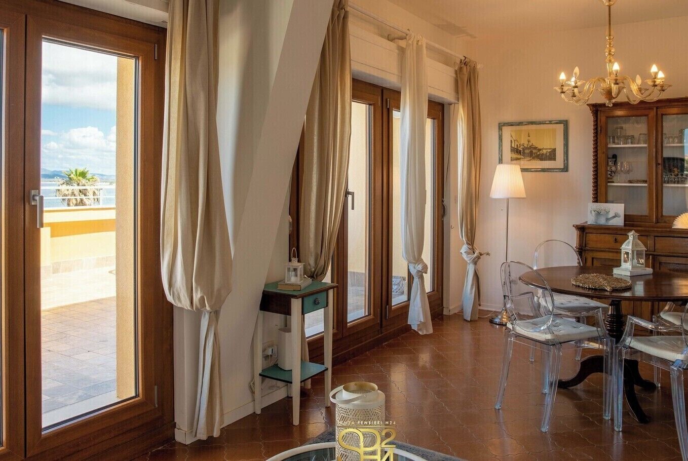 A room with large windows, a chandelier, a dining table with chairs, and a cabinet with glass doors.