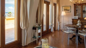 A room with large windows, a chandelier, a dining table with chairs, and a cabinet with glass doors. - Panoramic penthouse on the Gulf of Alghero 2 (Alghero)