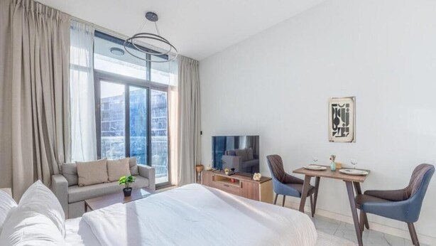Ett modernt hotellrum med en stor säng, en soffa, ett matbord med stolar, en TV och utsikt över staden genom fönstret.
