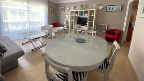 A modern living room with a round glass table, white and red chairs, a TV on a white stand, and a balcony with sheer curtains. - 2 rooms 8 av de l'ilette (Antibes)