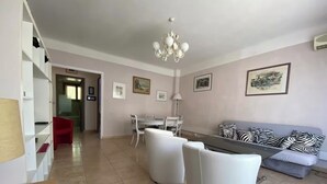 A modern living room with a sofa, two white armchairs, a dining table with chairs, and a chandelier. - 2 rooms 8 av de l'ilette (Antibes)
