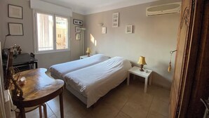 A bedroom with two beds, a desk, and a chair. There are wall-mounted air conditioning units and framed pictures on the walls. - 2 rooms 8 av de l'ilette (Antibes)
