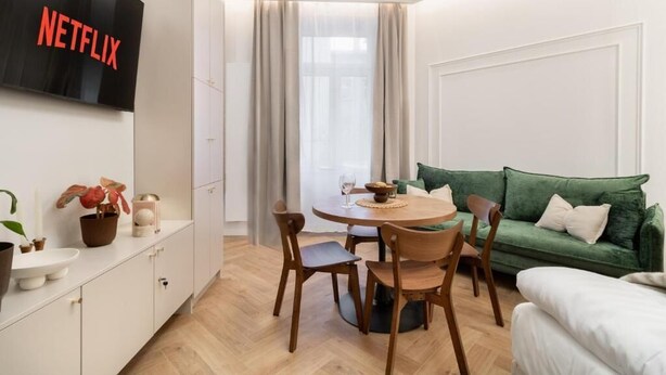 A modern living room with a green sofa, wooden dining table, and chairs. A flat-screen TV mounted on the wall displays the Netflix logo. - Malila Premium Apartments Estery Boutique (Kraków)