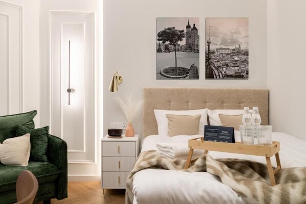 Una habitación de hotel con una cama, una mesita de noche, un sillón verde y dos cuadros colgados en la pared.
