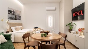 A modern, well-lit room with a bed, a dining table with chairs, a TV mounted on the wall, and a small potted plant. - Malila Premium Apartments Estery Boutique (Kraków)