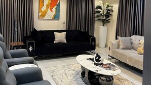 A modern living room with a black sofa, grey armchairs, a coffee table, and a large abstract painting. - Bateye Residence by Bedrock (Lagos)