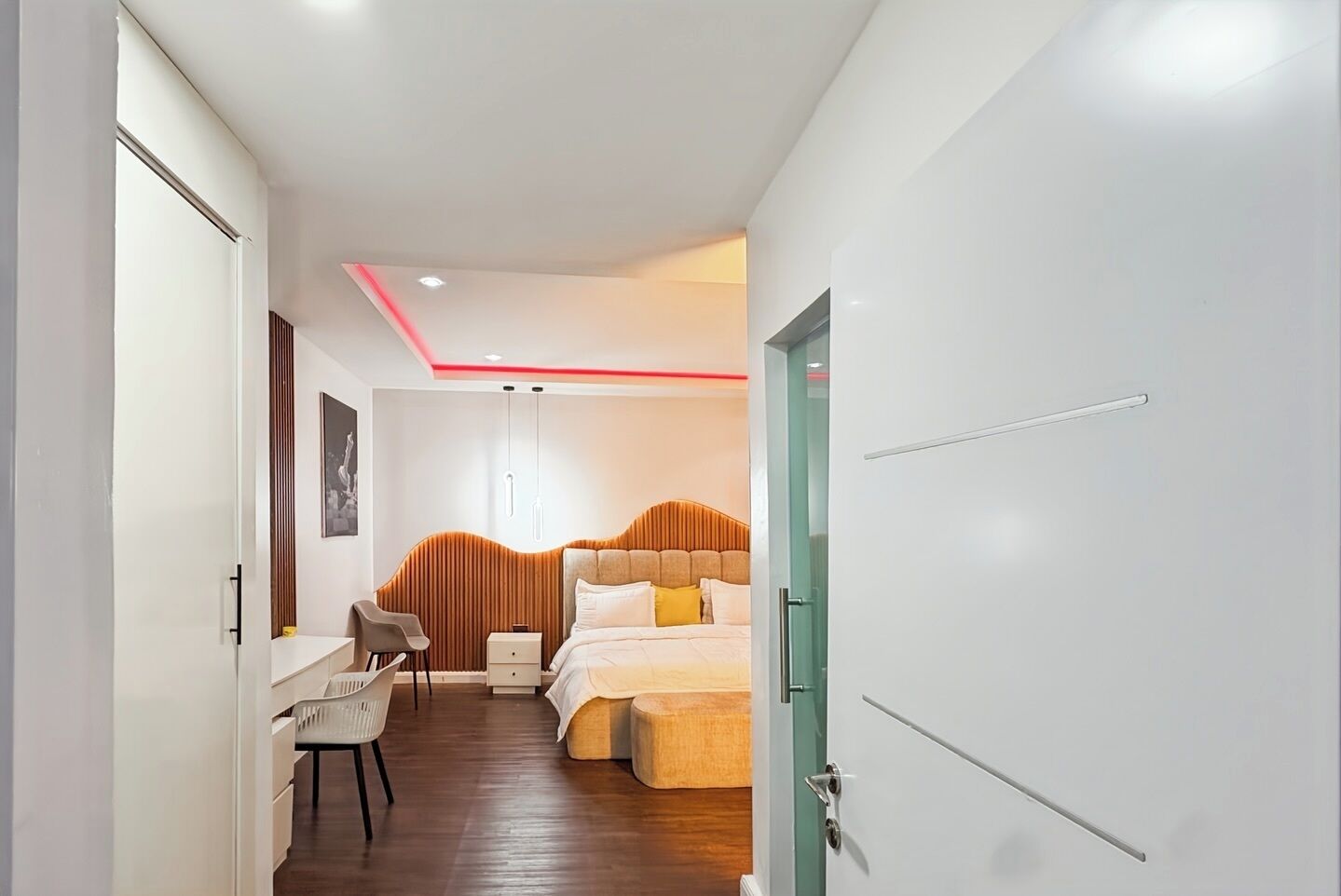 Una habitación de hotel moderna con cabecera de madera, una cama con ropa de cama blanca, un escritorio con silla y una mesita de noche.