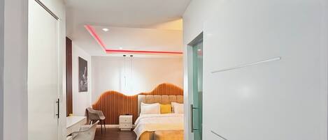 Una habitación de hotel moderna con cabecera de madera, una cama con ropa de cama blanca, un escritorio con silla y una mesita de noche.