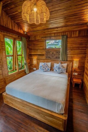 A wooden cabin bedroom with a large bed, a woven light fixture, and a window with curtains. - Prana Eco Wooden Villa Ubud (Ubud)