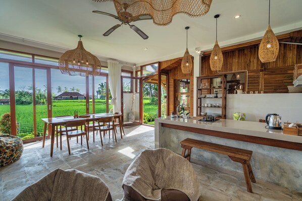 A spacious kitchen with a large island, wooden cabinets, and a view of a lush green landscape. - Prana Eco Wooden Villa Ubud (Ubud)
