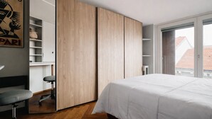A bedroom with a bed, a desk with a chair, a wardrobe, and a window with a view of buildings. - Hostmate - Milano - Burlamacchi 4 - Porta Romana  (Milano)