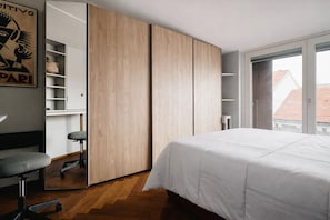 A bedroom with a bed, a desk with a chair, a wardrobe, and a window with a view of buildings. - Hostmate - Milano - Burlamacchi 4 - Porta Romana  (Milano)