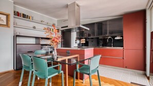 A modern kitchen with a glass dining table, teal chairs, and a central island. - Hostmate - Milano - Burlamacchi 4 - Porta Romana  (Milano)