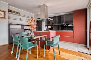 A modern kitchen with a glass dining table, teal chairs, and a central island. - Hostmate - Milano - Burlamacchi 4 - Porta Romana  (Milano)