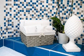 Un baño con piso de baldosas azules, una cesta de mimbre con toallas dobladas, una planta en maceta y un objeto decorativo blanco.