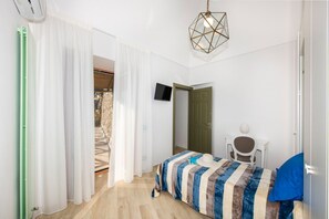 Un dormitorio con cama, televisión, silla y puerta que da a un balcón.