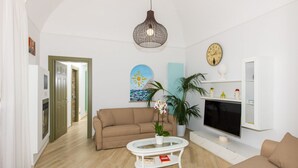 Un salon avec un canapé, une table basse, un téléviseur, une plante et une horloge murale.