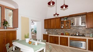 Une cuisine avec des meubles en bois, une table à manger avec des chaises, un four encastré et des luminaires suspendus.