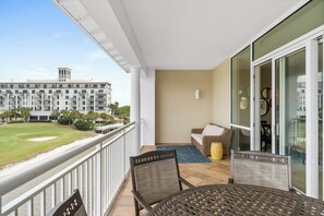 A balcony with a view of a golf course, a dining area with a table and chairs, and a large window. - Kiva Dunes Village A unit 301 (Gulf Shores)