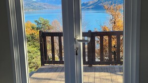 Una habitación con una cama, una terraza de madera y vistas a un lago y montañas a través de un ventanal.