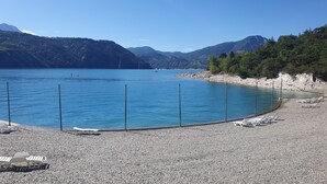 Un lago azul y transparente con orilla rocosa, rodeado de montañas.