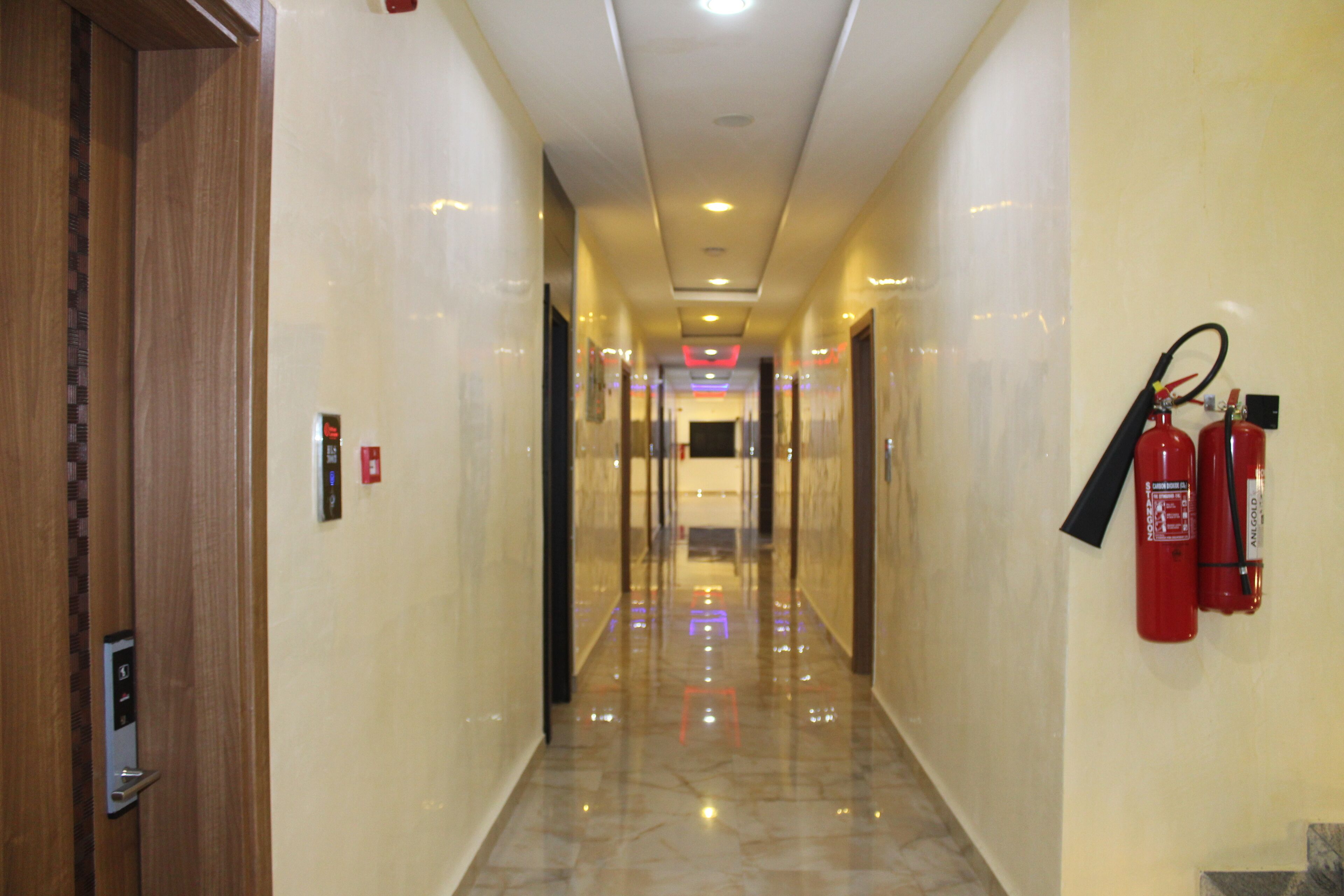 A hotel corridor with a shiny marble floor, wooden doors, and fire extinguishers on the wall.