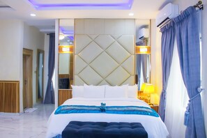 Una habitación de hotel moderna con una cama grande, un cabecero acolchado, una mesita de noche con una lámpara y un espejo amplio.