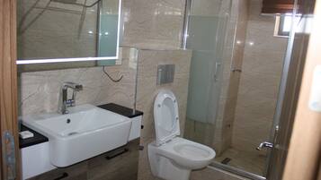 Une salle de bain avec un lavabo blanc, des toilettes, une douche en verre et un miroir au-dessus du lavabo.