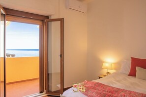 Ein Hotelzimmer mit Bett, Nachttisch mit Lampe, einer Schiebetür zum Balkon und einer Klimaanlage an der Wand.