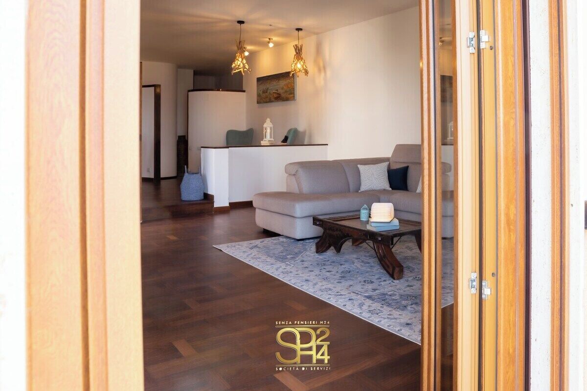 Een moderne woonkamer met een bank, een salontafel en een vloerkleed. In de achtergrond is een keuken met een eettafel en stoelen te zien.