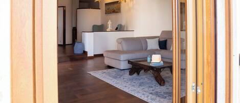 Een moderne woonkamer met een bank, een salontafel en een vloerkleed. In de achtergrond is een keuken met een eettafel en stoelen te zien.