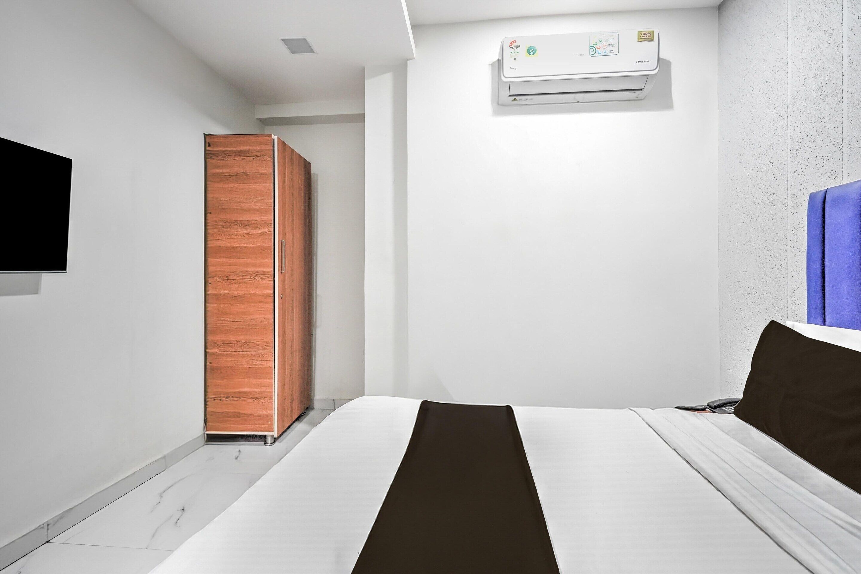 A modern hotel room with a bed, a wardrobe, and an air conditioning unit on the wall.