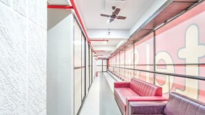 A corridor with red and purple seating, a ceiling fan, and a fire extinguisher. - Hotel O Sneh Rashmi Botanical Garden (Surat)