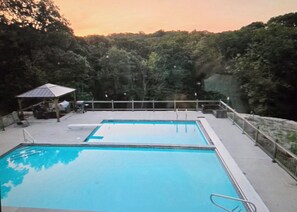 A swimming pool with a covered deck area, surrounded by trees.