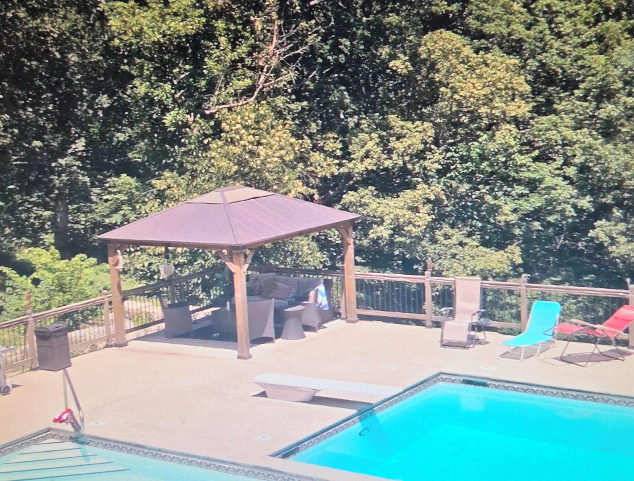 Un área de piscina con un pabellón, sillas de descanso y una terraza cercada.