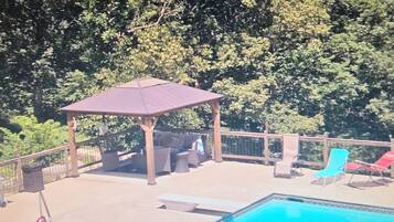 Un área de piscina con un pabellón, sillas de descanso y una terraza cercada.