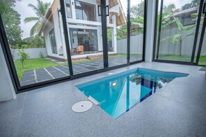 A modern house with a glass-enclosed swimming pool, a patio with outdoor furniture, and a view of a lush garden. - Gone4coastal Cabana B (Hikkaduwa)