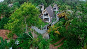 A house surrounded by dense tropical vegetation, with a sloped roof and a visible balcony.