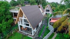 A modern, two-story house with a sloped roof, surrounded by lush greenery and a small garden. - Gone4coastal Cabana B (Hikkaduwa)