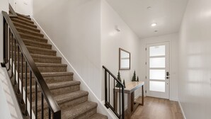 Un escalier dont les marches sont recouvertes de moquette et qui possède des rampes noires, menant à une porte dont les panneaux sont en verre dépoli.