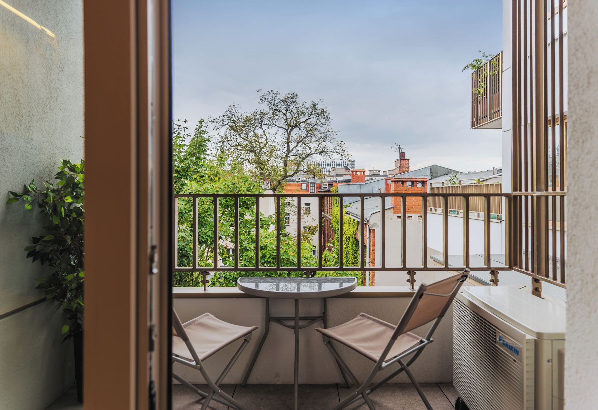 A balcony with a table and two chairs, overlooking a cityscape with buildings and trees.