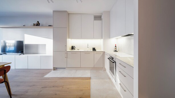 A modern kitchen with white cabinetry, a wooden dining table, and a flat-screen TV. - RentPlanet - Apartament Dąbrowskiego (Poznań)
