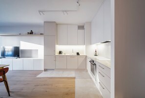 Una cocina moderna con armarios blancos, una mesa de comedor de madera y un televisor de pantalla plana.