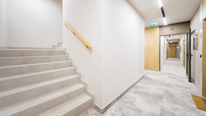 A modern hotel corridor with a staircase, a wooden door, and a hallway leading to a room. - RentPlanet - Apartament Dąbrowskiego (Poznań)