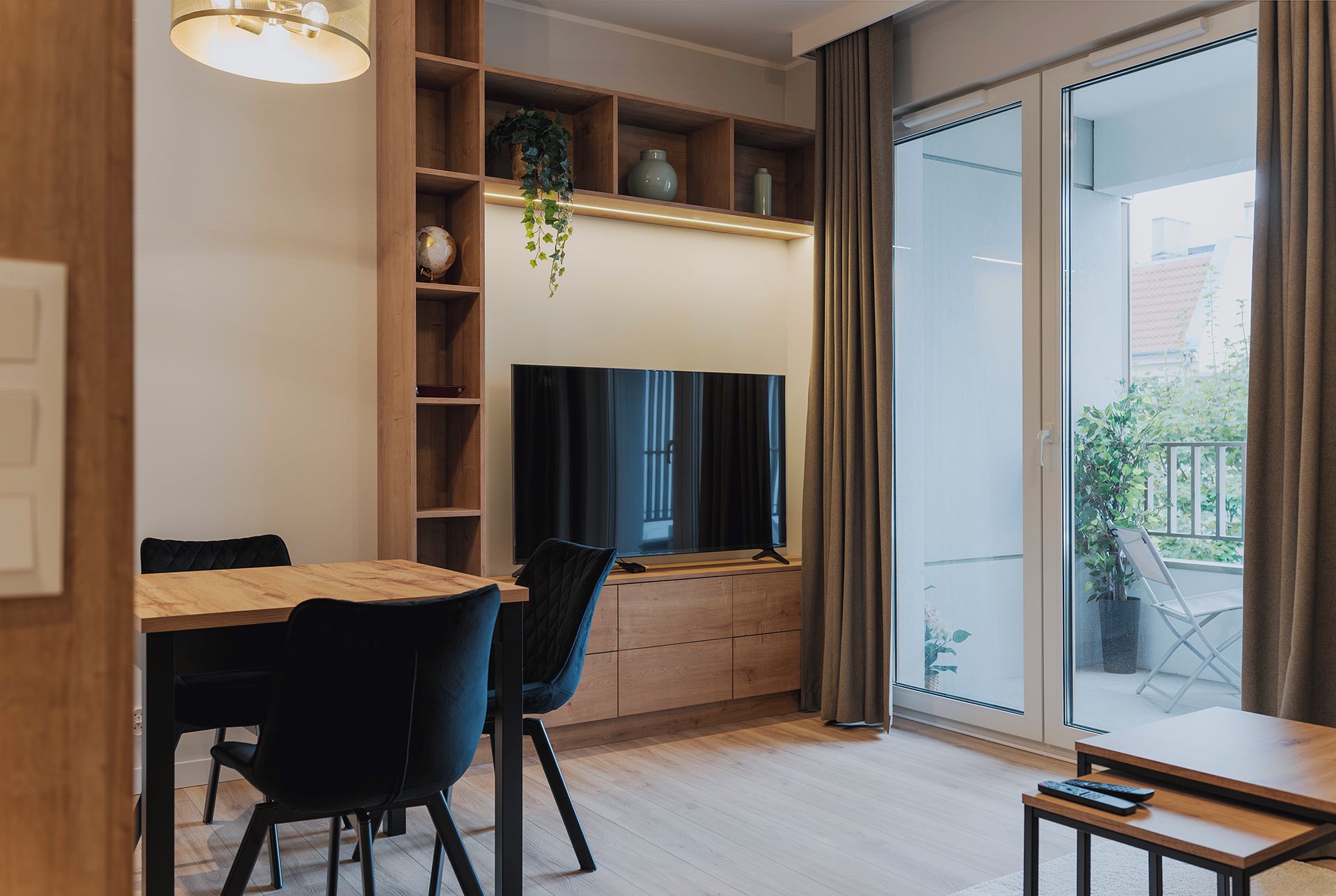 A modern living room with a dining table, chairs, a television, and a large window with curtains.