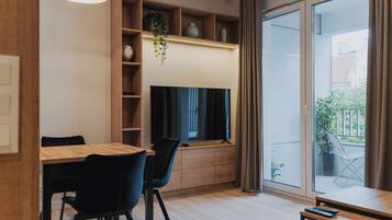 A modern living room with a dining table, chairs, a television, and a large window with curtains.